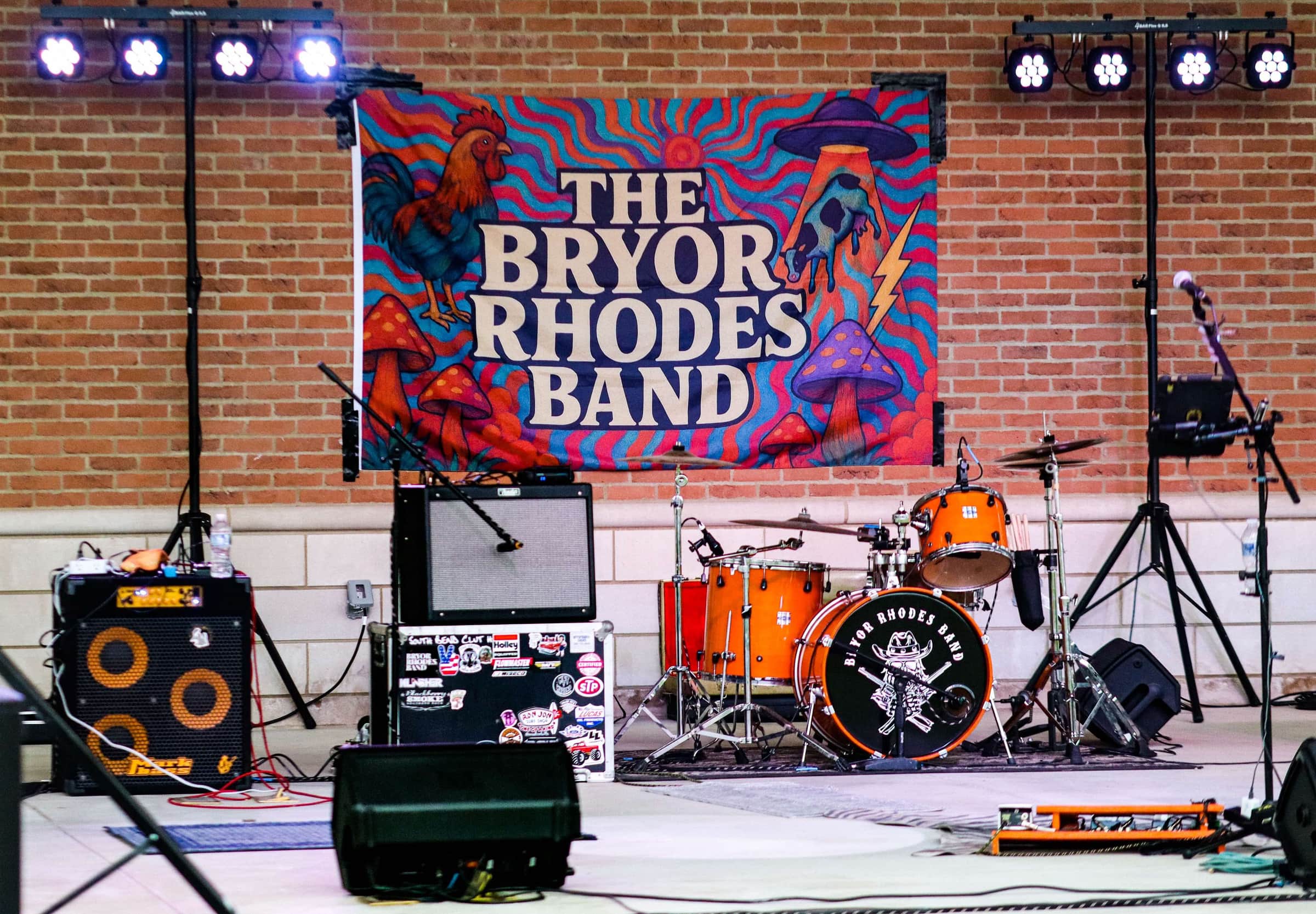 The Bryor Rhodes Band stage, rooster banner hung on a brick wall behind the drum kit
